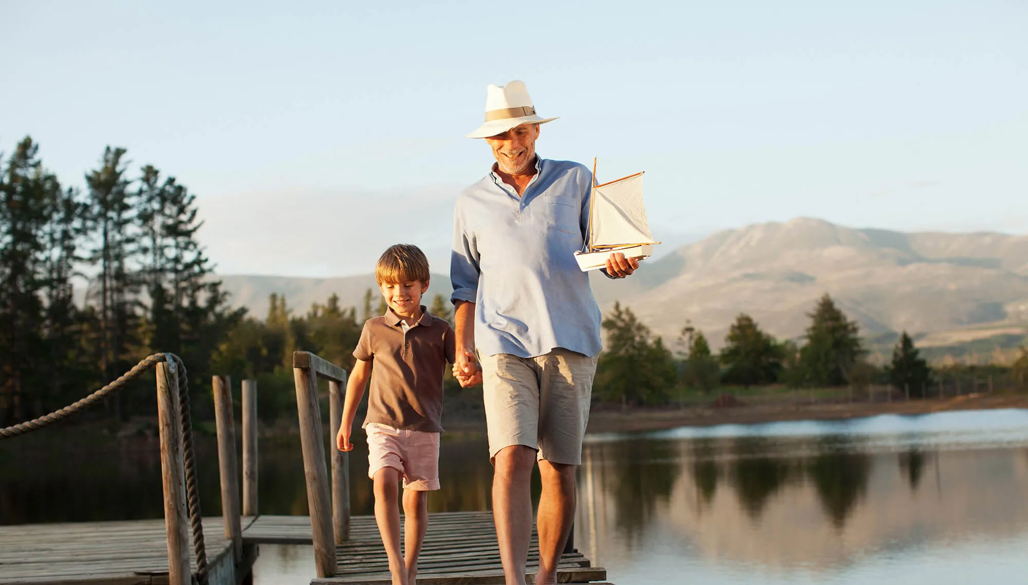 Grandfather grandson holding hands walking along dock over lake